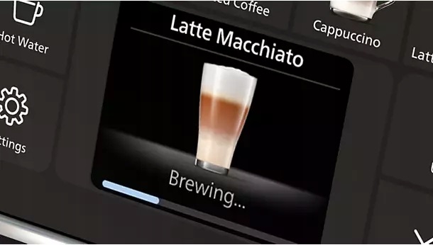 Zbliżenie na włączony wyświetlacz ekspresu Philips 5500 LatteGo. Wyświetlacz pokazuje napój Latte Macchiato oraz napis Brewing... i pasek postępu.