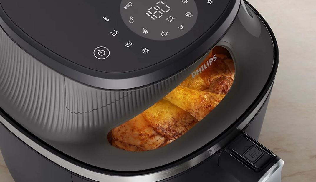 Крупный план верхней панели управления черной аэрофритюрницы Philips Ovi NA322. Панель сенсорная и включает в себя цифровой дисплей с температурой «180°C» и значками программ приготовления. В нижней части фотографии вы можете видеть жареное мясо в ящике фритюрницы.
