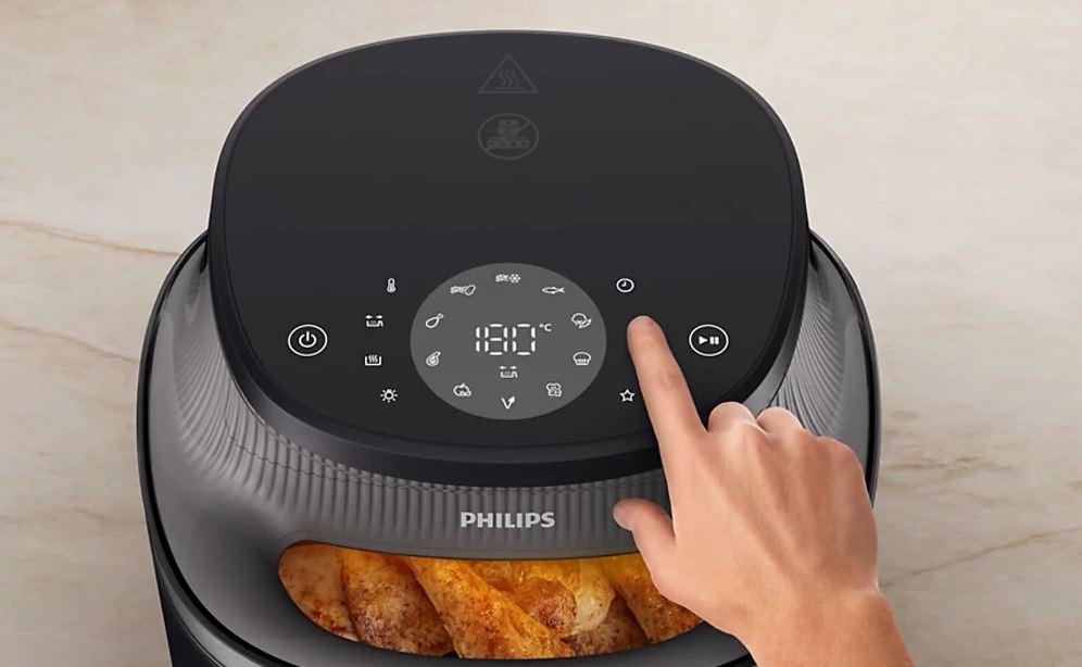 Крупный план верхней панели управления черной аэрофритюрницы Philips Ovi NA322, управляемой вручную. Панель сенсорная и включает в себя цифровой дисплей с температурой «180°C» и значками программ приготовления. В нижней части фотографии вы можете видеть жареное мясо в ящике фритюрницы.